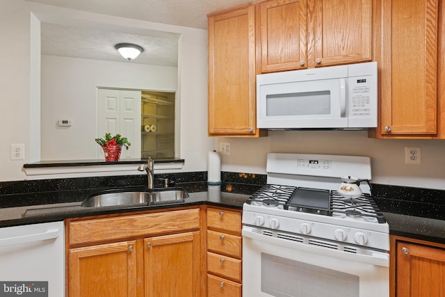 kitchen with dark stone countertops, a textured ceiling, a sink, and white appliances