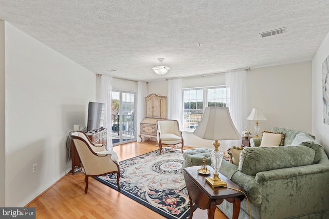 living room featuring a textured ceiling, visible vents, and light wood-type flooring