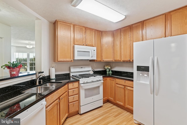 kitchen with light wood-type flooring, white appliances, a textured ceiling, and a sink