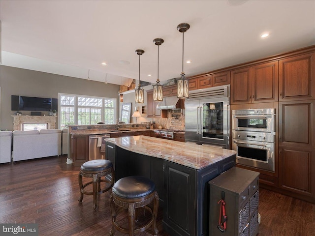kitchen featuring a sink, stainless steel appliances, a peninsula, a kitchen island, and under cabinet range hood