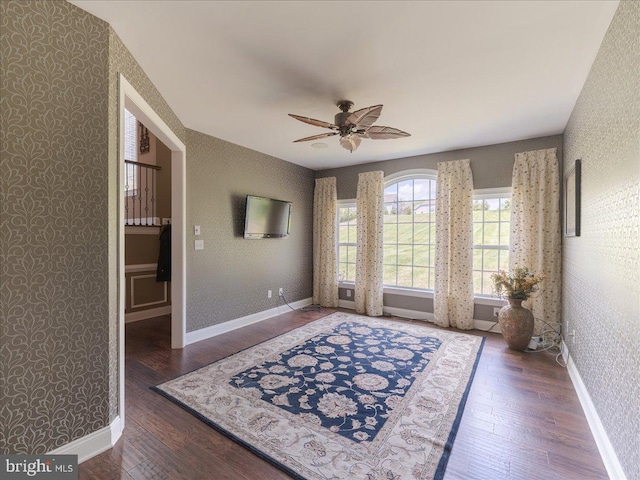 interior space featuring baseboards, a ceiling fan, wallpapered walls, and wood finished floors