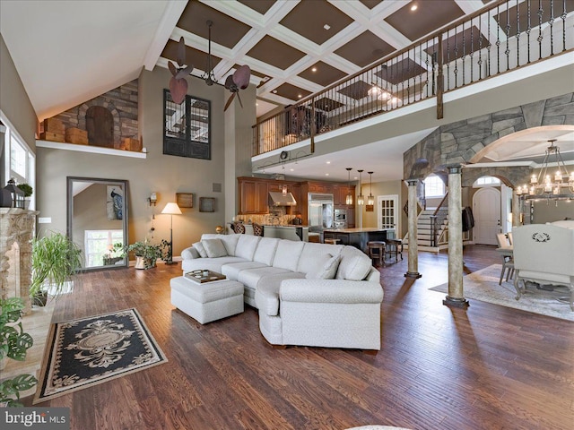 living room with dark wood-style flooring, a towering ceiling, ornate columns, arched walkways, and a notable chandelier