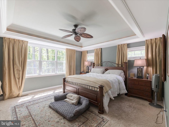 carpeted bedroom featuring a ceiling fan, baseboards, multiple windows, and a raised ceiling