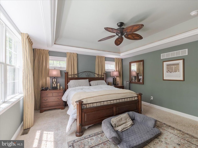 bedroom featuring a ceiling fan, light colored carpet, visible vents, baseboards, and a tray ceiling