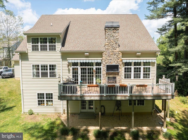 rear view of house with french doors, a wooden deck, a shingled roof, and a lawn