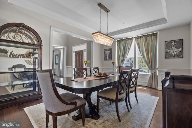 dining space with a tray ceiling, ornamental molding, wood finished floors, and a wainscoted wall