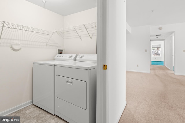 clothes washing area with laundry area, baseboards, washer and dryer, and light carpet