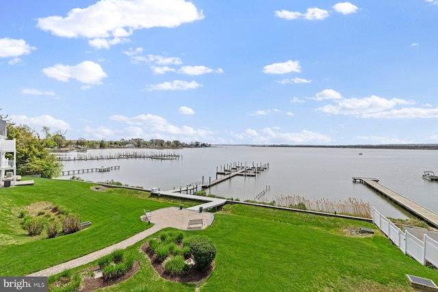 view of dock with fence, a water view, and a lawn