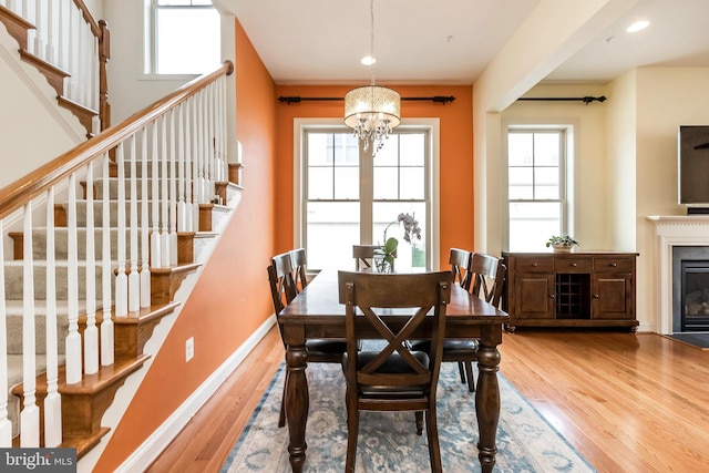 dining area with stairs, wood finished floors, baseboards, a notable chandelier, and a glass covered fireplace