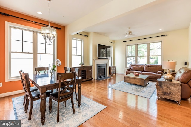 dining area featuring ceiling fan with notable chandelier, a fireplace with flush hearth, baseboards, light wood-style floors, and recessed lighting