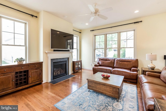 living area with a ceiling fan, recessed lighting, light wood finished floors, and a fireplace with flush hearth