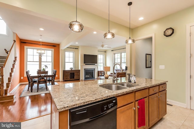 kitchen with a sink, black dishwasher, a center island with sink, a fireplace, and hanging light fixtures
