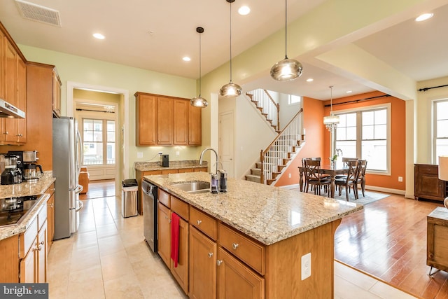 kitchen featuring a sink, stainless steel appliances, light stone counters, visible vents, and an island with sink
