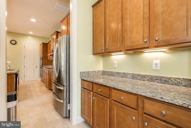 kitchen with brown cabinetry, freestanding refrigerator, light stone counters, visible vents, and recessed lighting