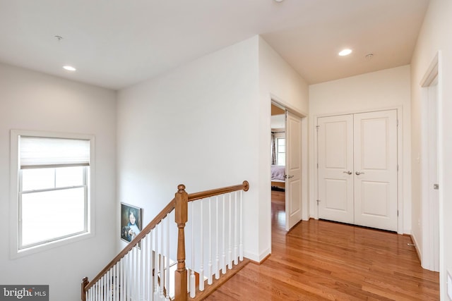 hallway with baseboards, light wood-type flooring, an upstairs landing, and recessed lighting