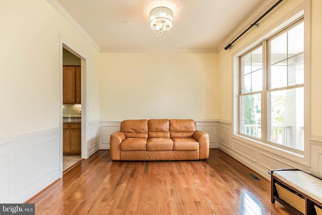 living area featuring a decorative wall, a wainscoted wall, ornamental molding, a chandelier, and light wood-style floors