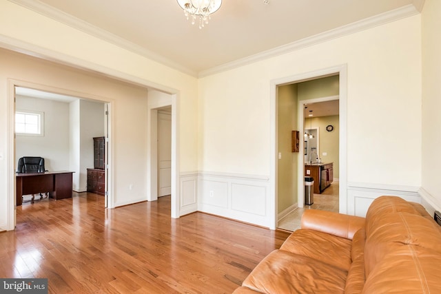 living room with ornamental molding, an inviting chandelier, light wood-type flooring, and a wainscoted wall