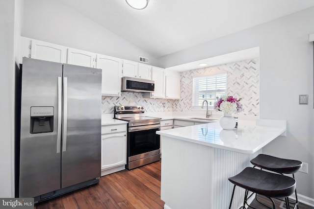 kitchen with a peninsula, a kitchen breakfast bar, dark wood-style floors, white cabinetry, and stainless steel appliances