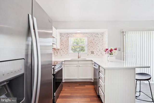 kitchen featuring dark wood-style flooring, a peninsula, a breakfast bar, a sink, and stainless steel appliances