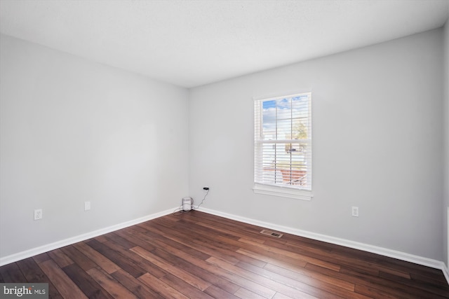 unfurnished room featuring baseboards, dark wood-style floors, and visible vents