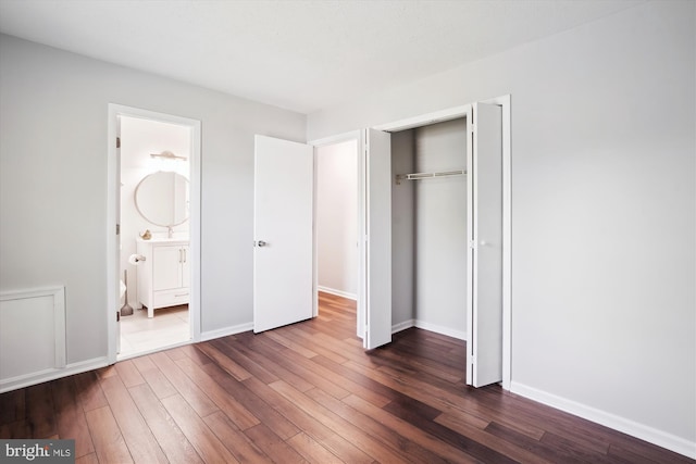 unfurnished bedroom with baseboards, a closet, dark wood-style flooring, and ensuite bath
