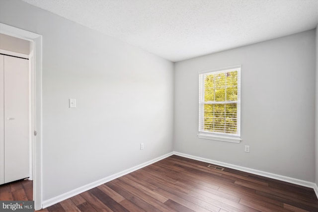 spare room featuring baseboards, a textured ceiling, dark wood-style floors, and visible vents