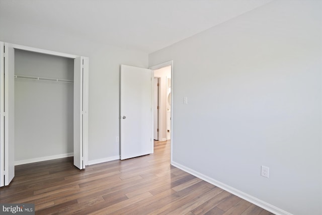 unfurnished bedroom featuring baseboards, wood finished floors, and a closet