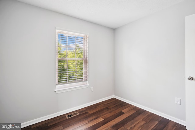 spare room with visible vents, baseboards, and dark wood finished floors
