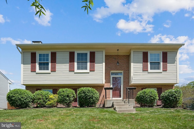 bi-level home with brick siding, a chimney, and a front lawn