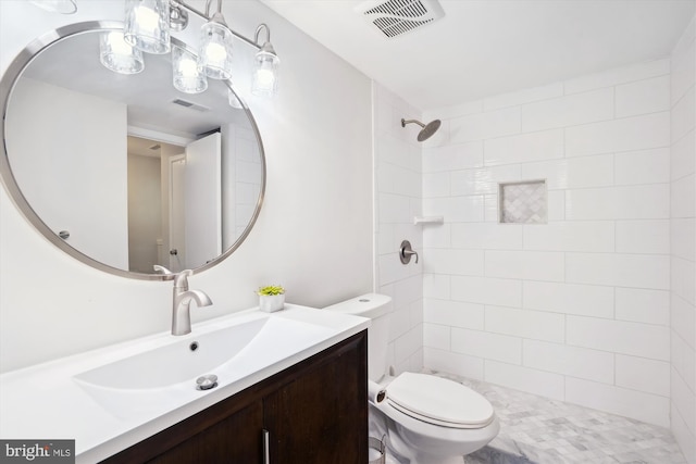 bathroom featuring toilet, visible vents, a tile shower, and vanity