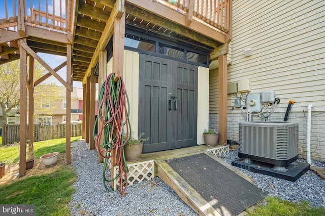 property entrance with fence, a wooden deck, and cooling unit