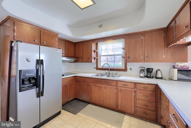 kitchen with brown cabinetry, white microwave, under cabinet range hood, stainless steel fridge with ice dispenser, and a sink