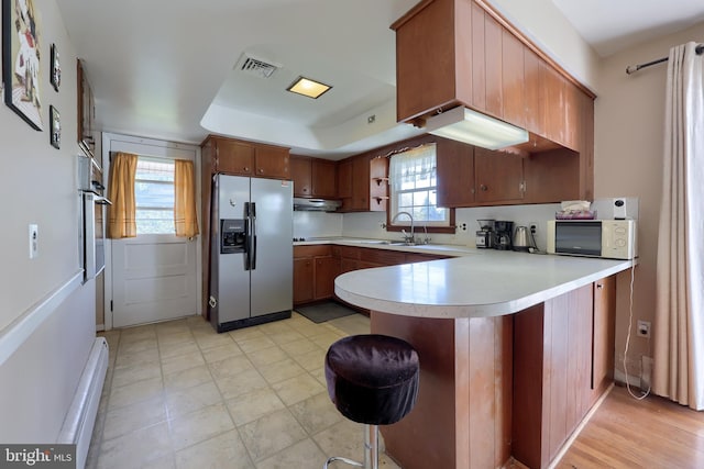 kitchen featuring appliances with stainless steel finishes, a sink, light countertops, a peninsula, and under cabinet range hood