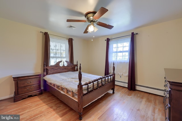 bedroom with a baseboard radiator, multiple windows, light wood finished floors, and visible vents