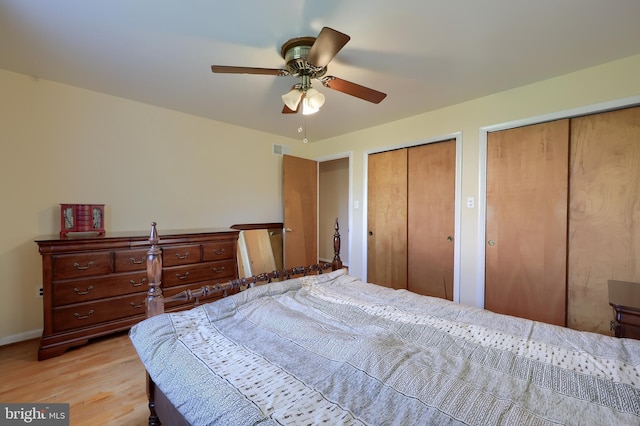 bedroom featuring a ceiling fan, visible vents, light wood-type flooring, baseboards, and two closets