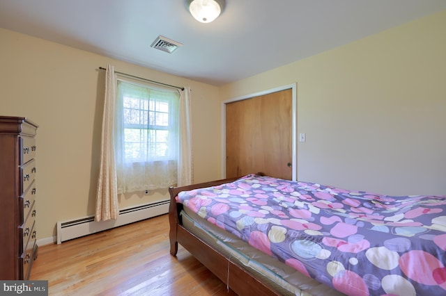 bedroom with a baseboard radiator, light wood finished floors, and visible vents