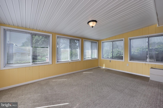 unfurnished sunroom featuring a healthy amount of sunlight, carpet, vaulted ceiling, and wooden walls