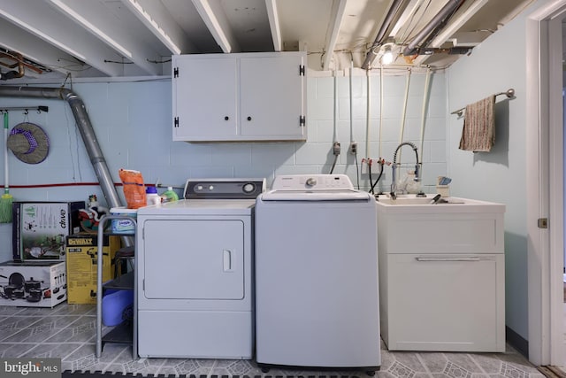 clothes washing area with cabinet space, concrete block wall, a sink, and washing machine and clothes dryer