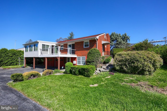 view of front of home featuring an attached garage, brick siding, a sunroom, a front yard, and driveway