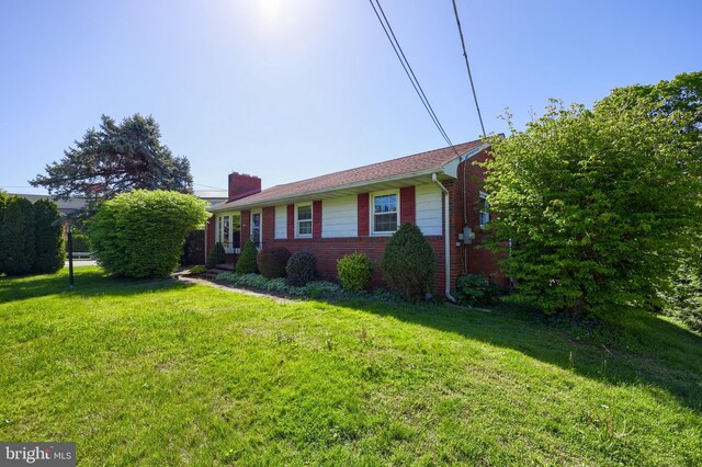 view of front facade featuring brick siding, a chimney, and a front yard