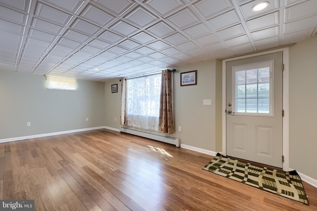 foyer entrance with baseboards, a baseboard radiator, wood finished floors, and a healthy amount of sunlight
