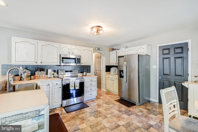 kitchen featuring decorative backsplash, stone finish floor, arched walkways, a sink, and stainless steel appliances