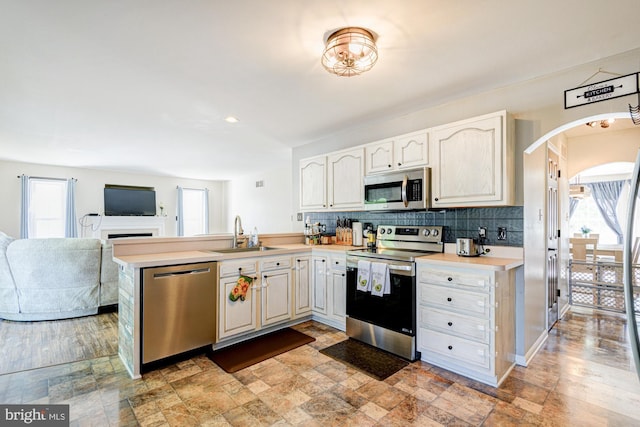 kitchen with decorative backsplash, a peninsula, light countertops, a sink, and appliances with stainless steel finishes