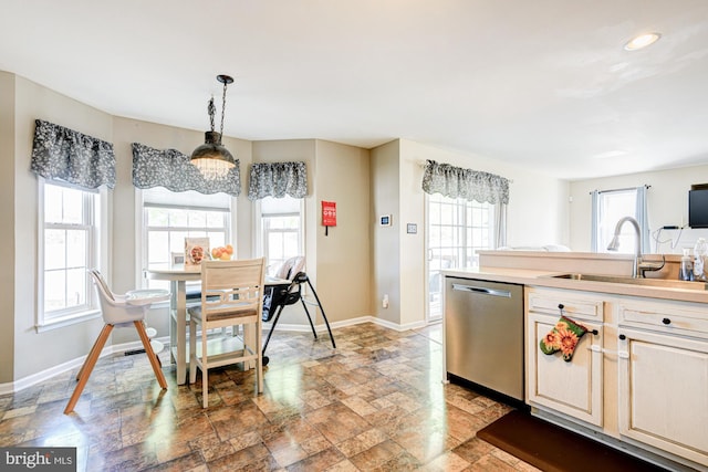 kitchen with stone tile floors, baseboards, a sink, dishwasher, and hanging light fixtures