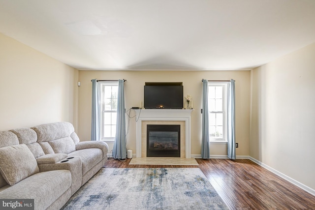 living area featuring a tiled fireplace, baseboards, and wood finished floors