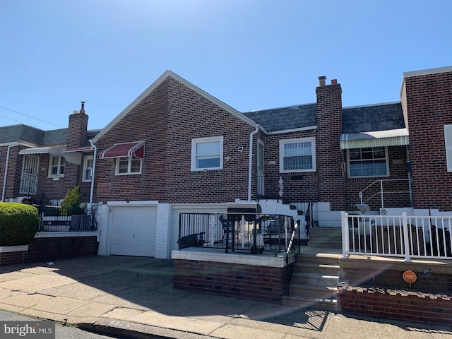 rear view of property featuring concrete driveway, a chimney, a garage, and brick siding