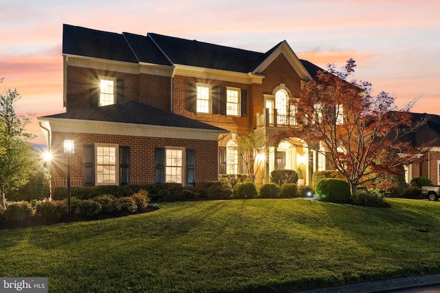 colonial home featuring a yard, brick siding, and a balcony