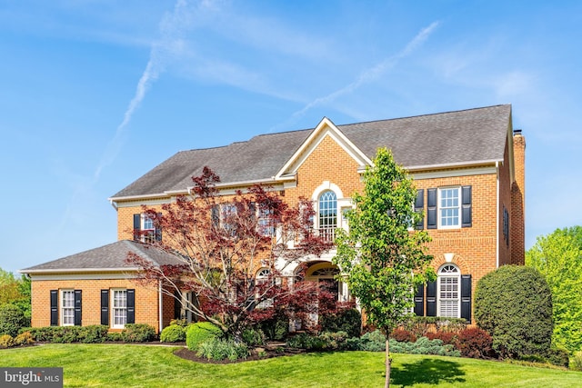 view of front of property featuring roof with shingles, a front lawn, and brick siding
