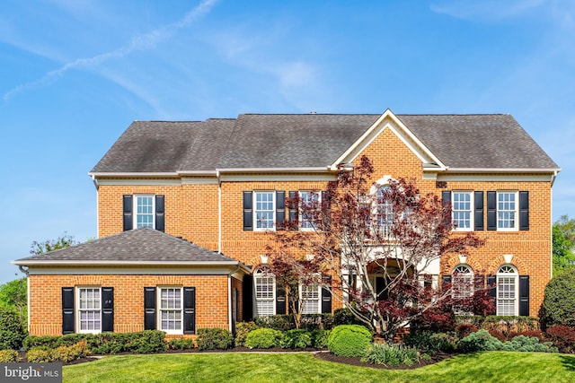 view of front of property featuring brick siding, roof with shingles, and a front yard