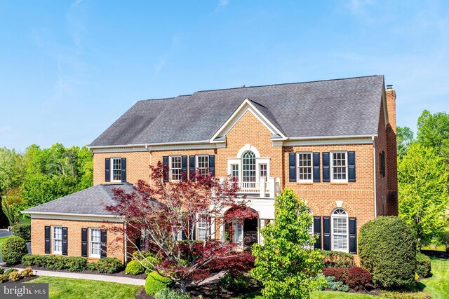 colonial home with brick siding, a shingled roof, and a chimney